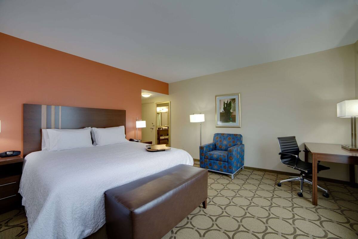 A hotel room with a bed, a chair, a desk, and a lamp.