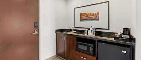 Una kitchenette compacta con microondas, cafetera y botellas de agua.