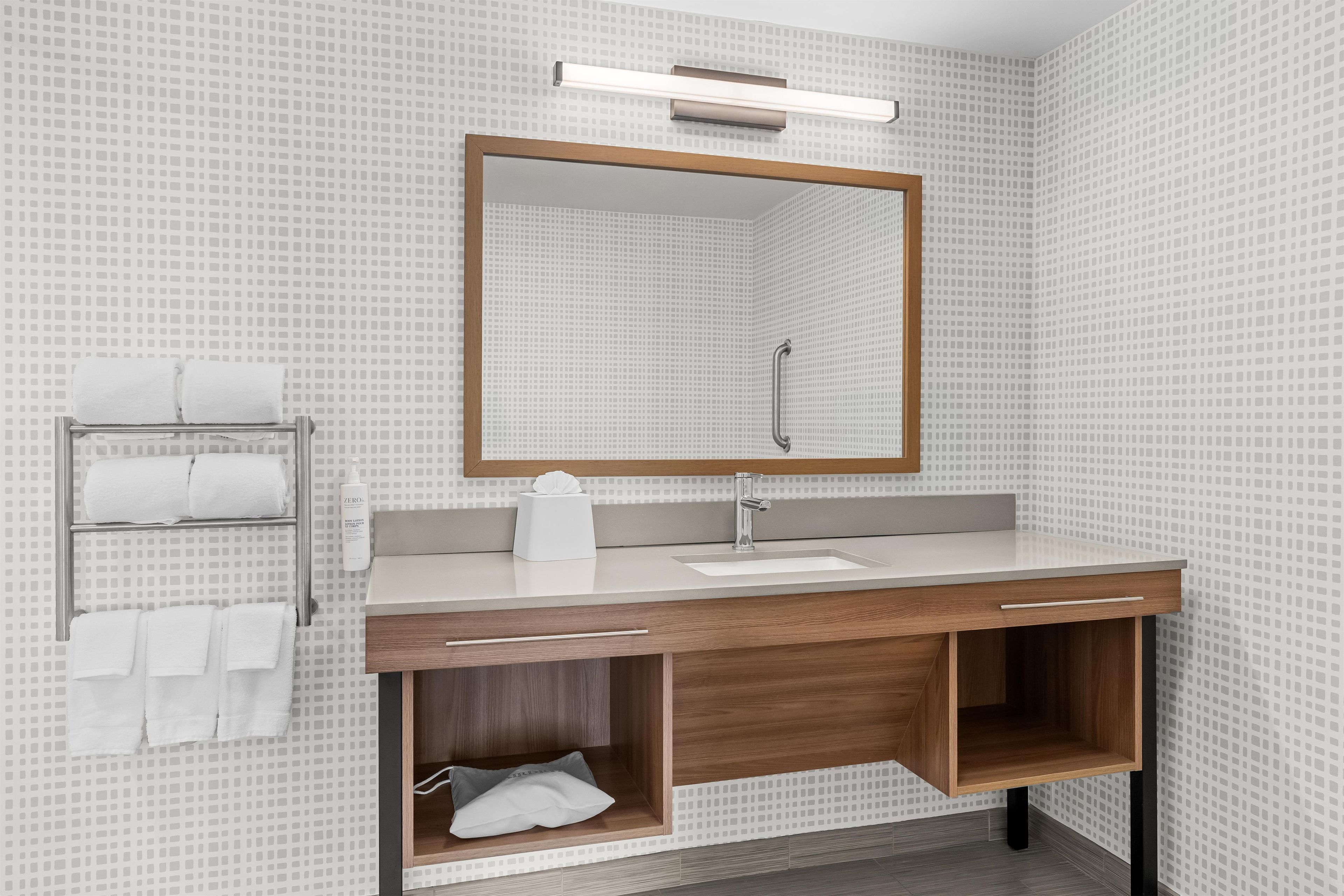 Ein modernes Badezimmer mit Waschtisch, Spiegel, Handtuchhalter und Waschbecken.