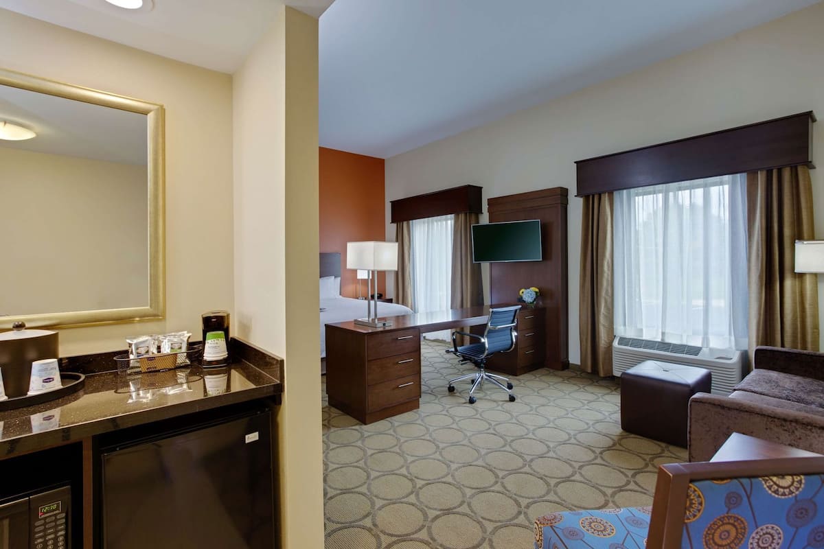 A hotel room with a large mirror, a desk with a chair, a bed, a TV, and a small sofa.