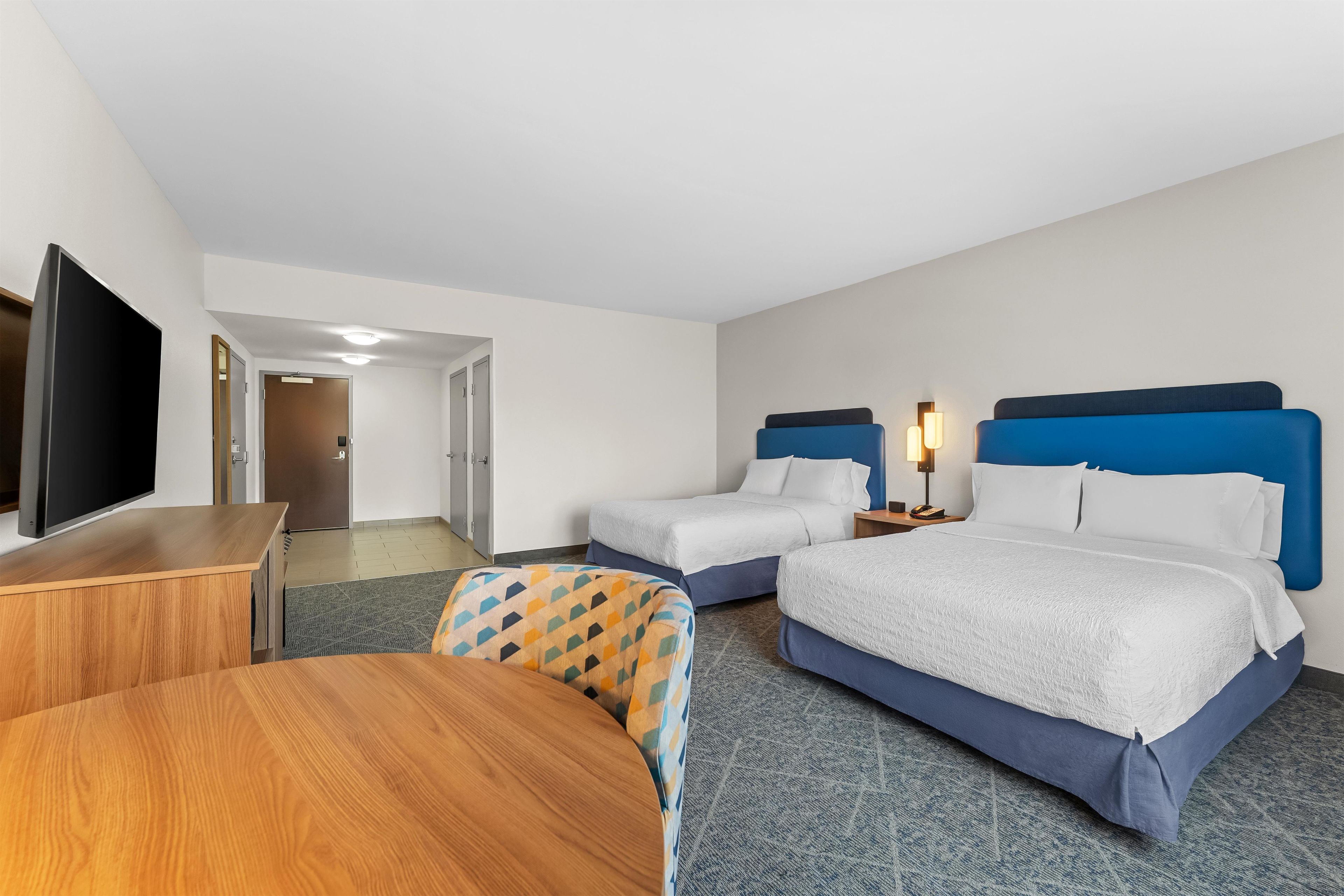 Quarto de hotel com duas camas, televisão, escrivaninha e uma cadeira.