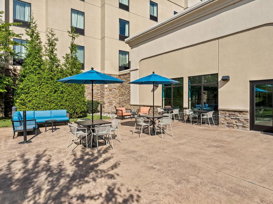 An outdoor patio area with tables and chairs, blue umbrellas, and a stone wall.