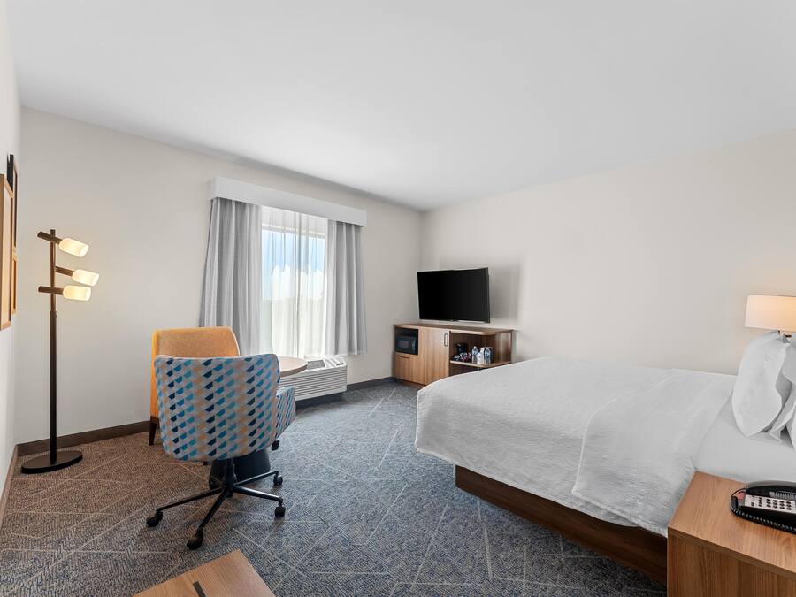 A hotel room with a bed, a desk, a chair, a television, and a bedside table with a phone.