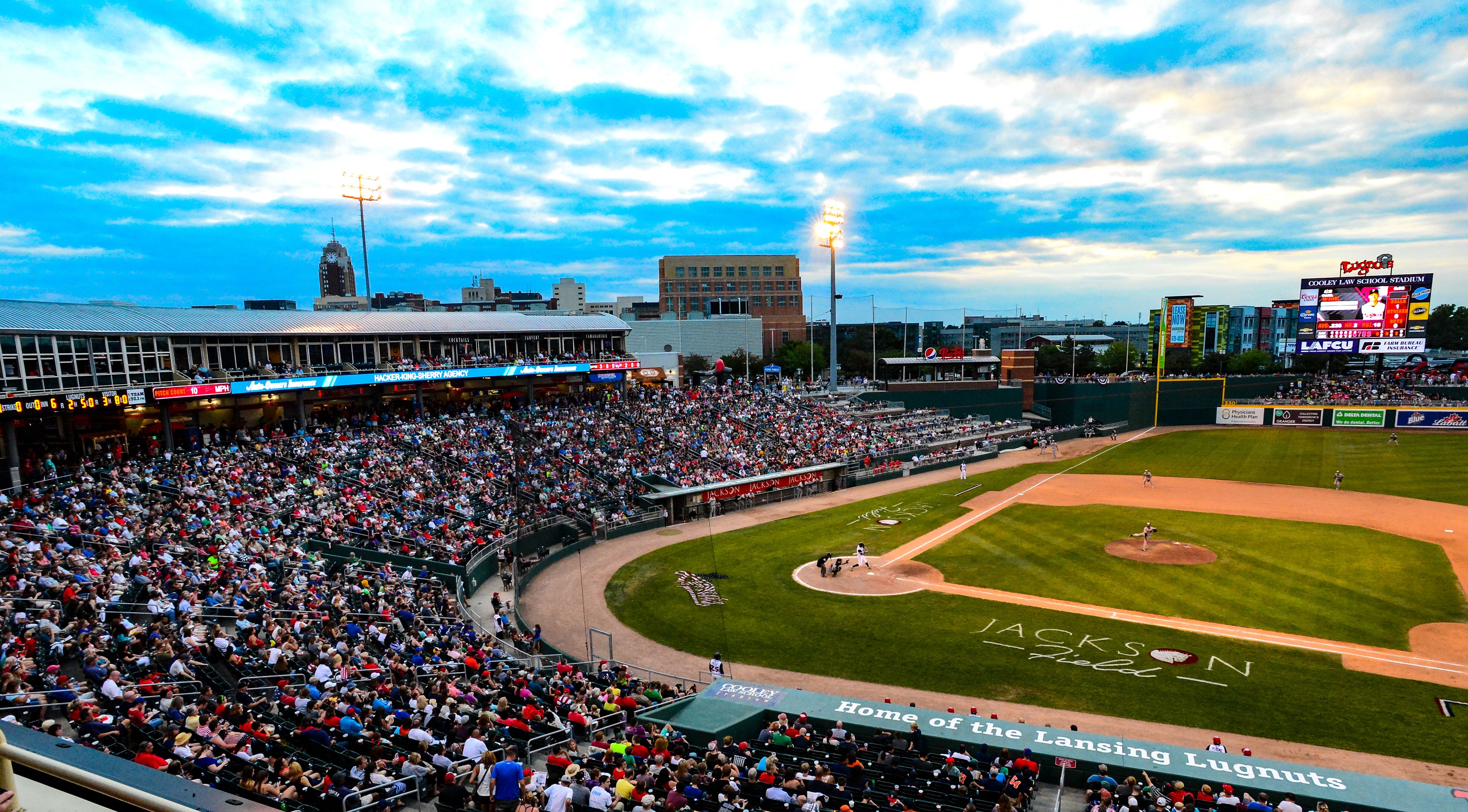 A baseball stadium with a large crowd, a scoreboard, and advertisements.