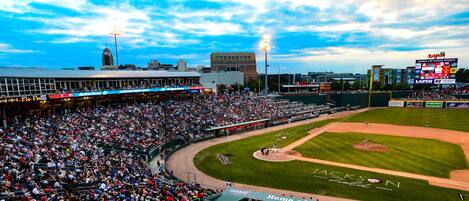 A baseball stadium with a large crowd, a scoreboard, and advertisements.