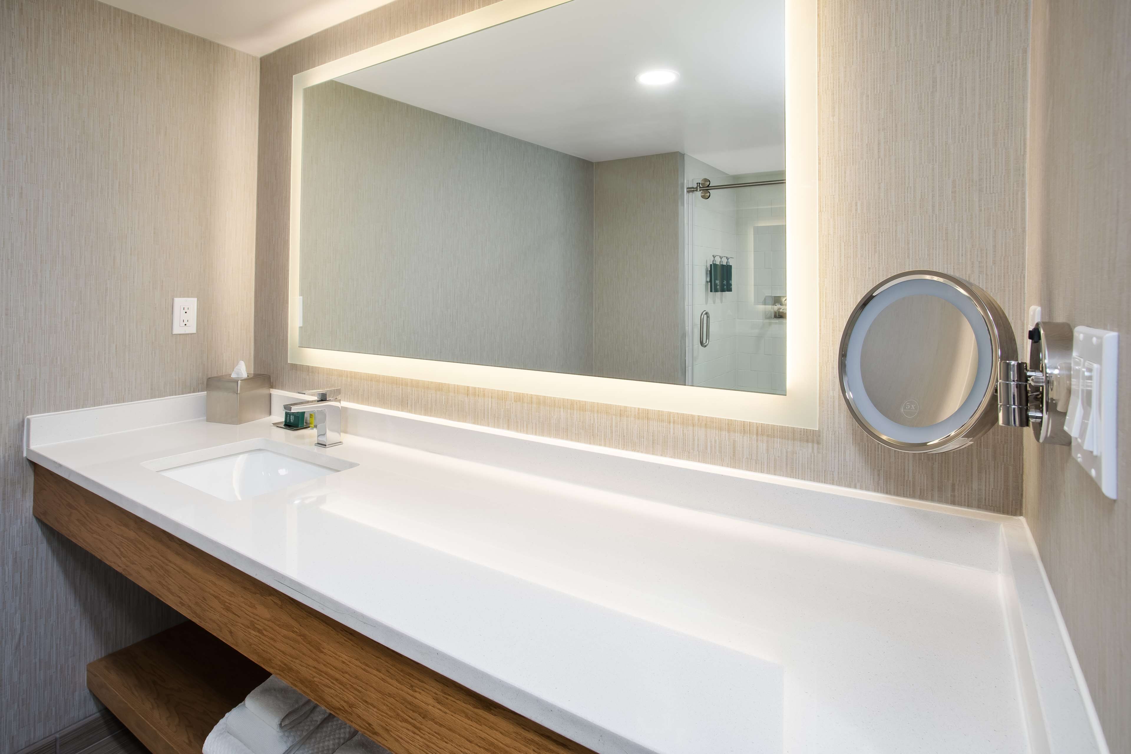 A modern bathroom with a large mirror, two sinks, and a wooden vanity.