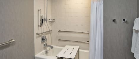 Un baño moderno con ducha a nivel, barras de apoyo y una bañera blanca.