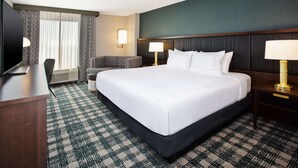 A hotel room with a large bed, a desk with a television, a chair, and two bedside lamps. - DoubleTree by Hilton Lansing (Lansing)