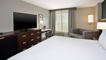 A hotel room with a large bed, a desk with a chair, a television, and a lamp.