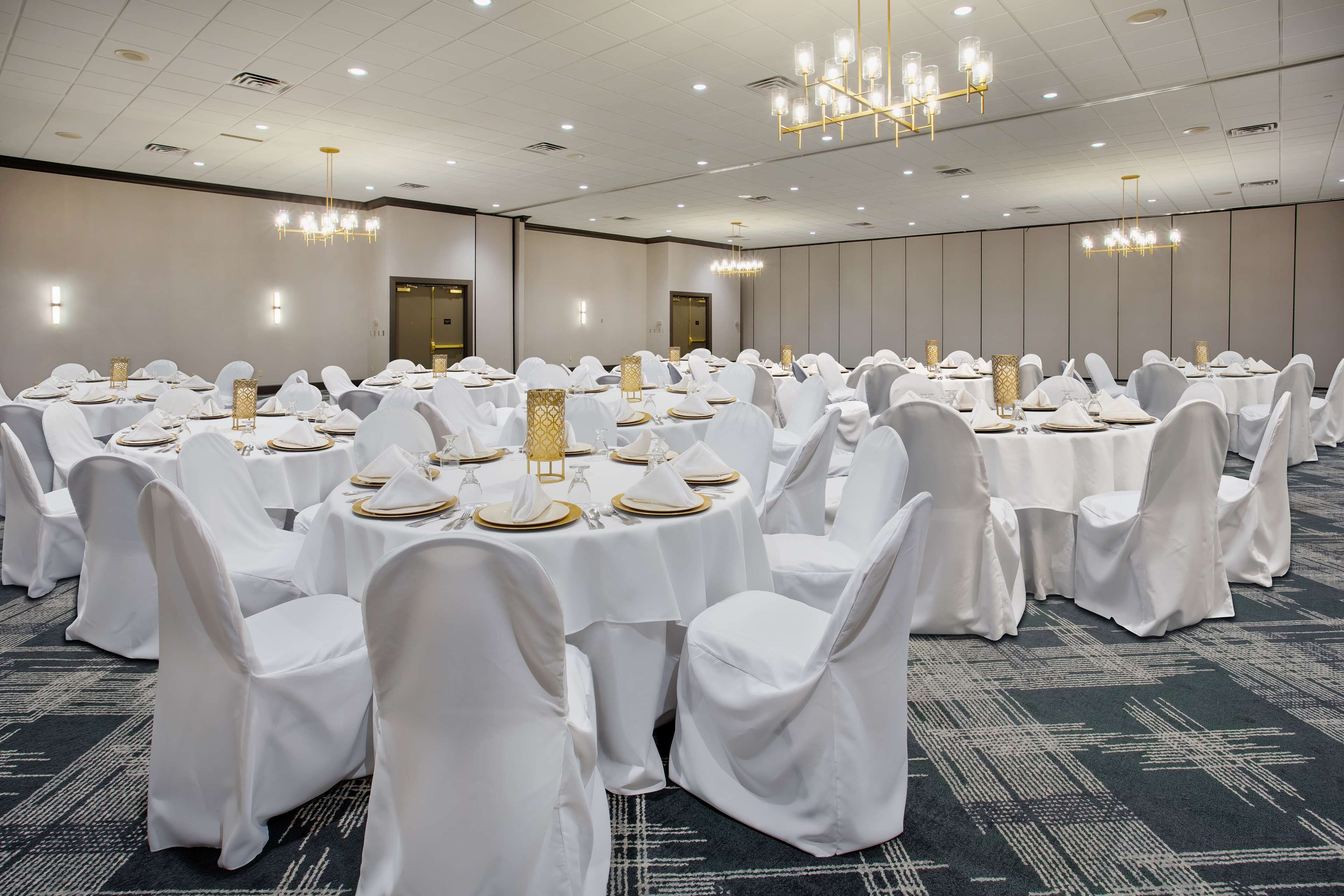 A banquet hall with round tables set for dining, white chairs, and chandeliers.