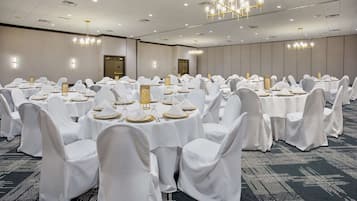 A banquet hall with round tables set for dining, white chairs, and chandeliers.