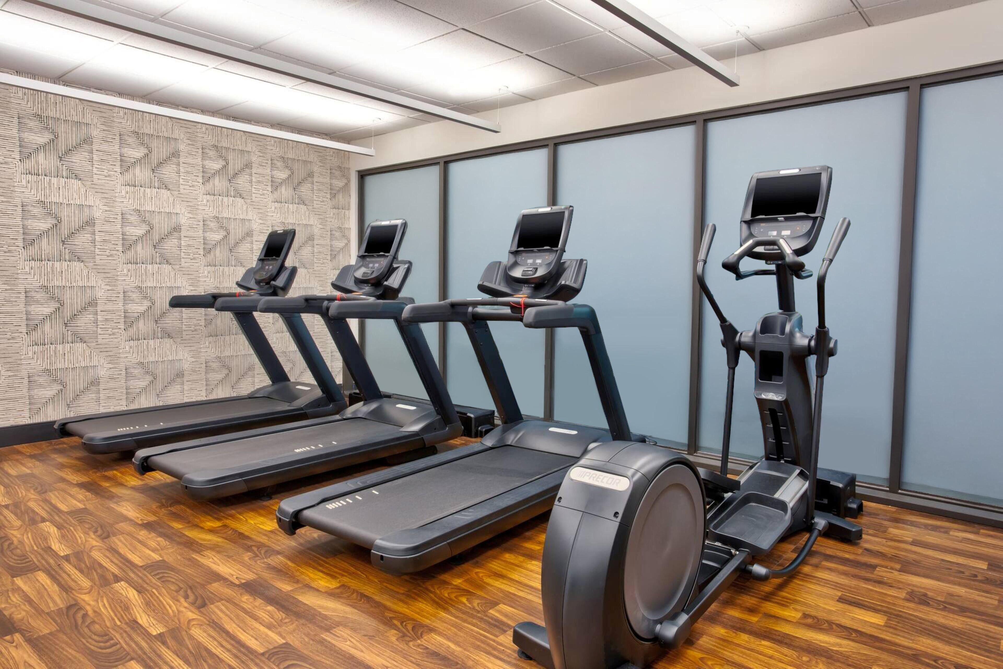 A fitness room with treadmills and elliptical machines, wooden flooring, and patterned wall decor.