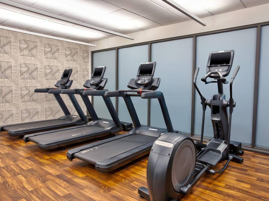 A fitness room with treadmills and elliptical machines, wooden flooring, and patterned wall decor.
