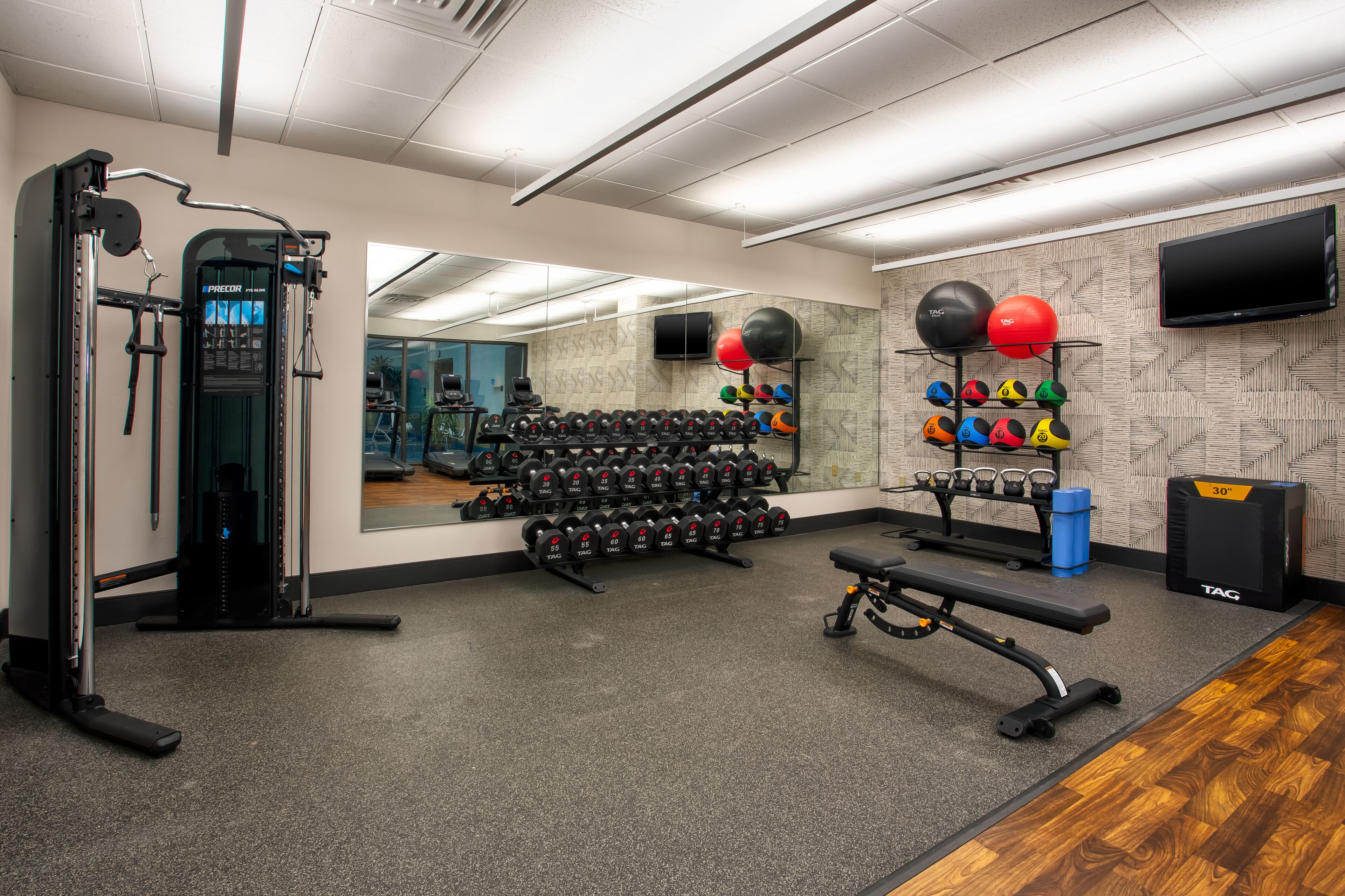 A gym with weightlifting equipment, a bench, a mirror, and a TV on the wall.