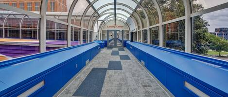 A covered walkway with blue railings and a checkered floor leading to the Lansing Center.