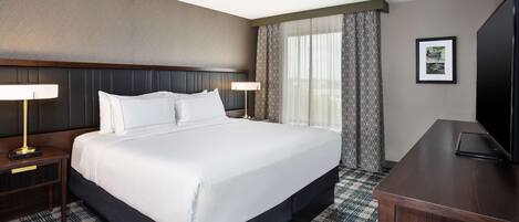 Habitación de hotel con una cama grande, dos mesitas de noche con lámparas, un escritorio y un televisor.