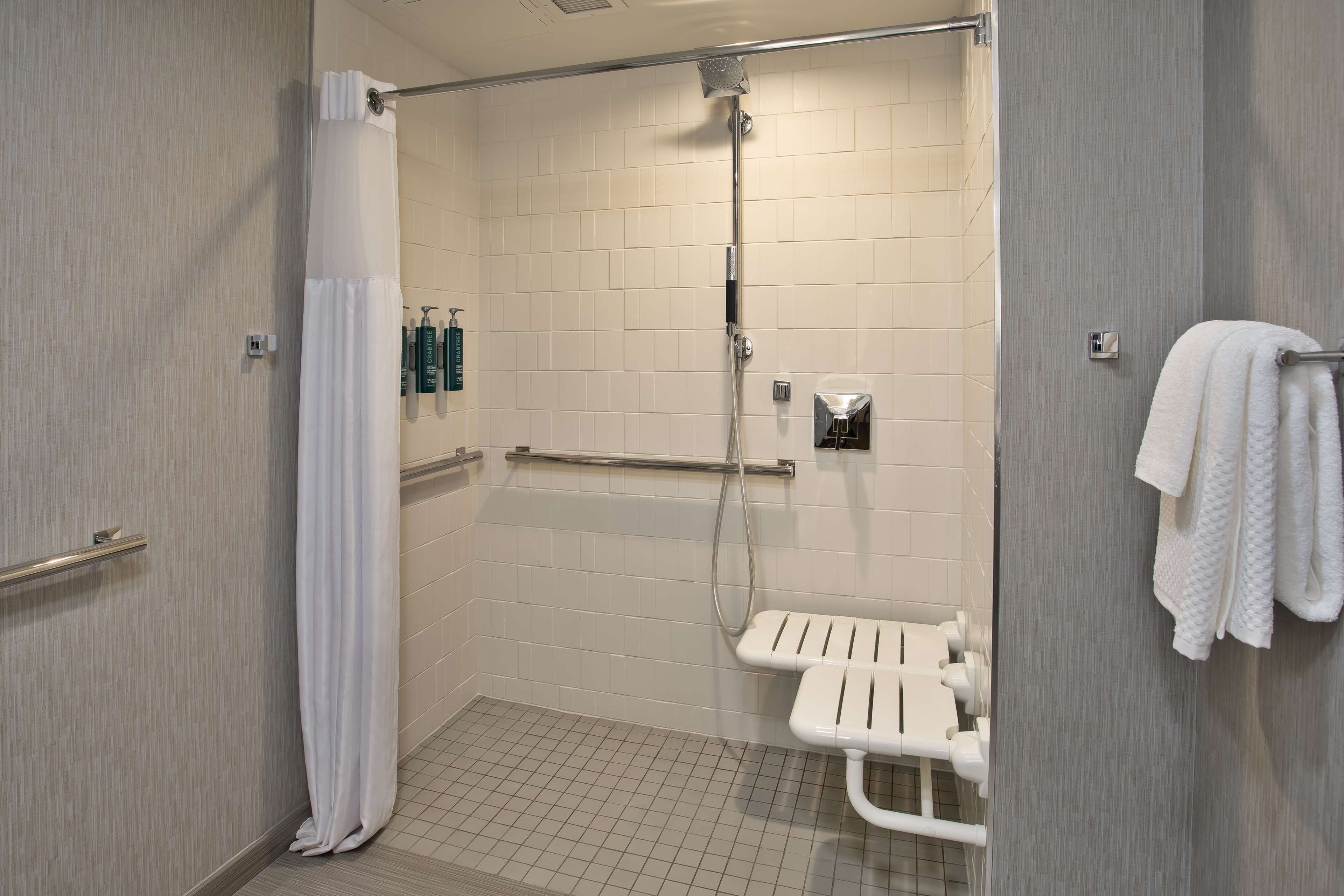 A modern bathroom with a shower, grab bars, a white toilet, and a towel rack.