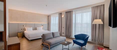 A modern hotel room with a bed, sofa, armchair, and a small coffee table.