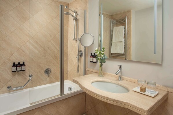 Un baño moderno con bañera, ducha y lavabo. Hay artículos de aseo en la pared y un espejo sobre el lavabo.