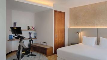 Habitación de hotel con cama, escritorio con computadora, pupitre con silla, caminadora y estantería.