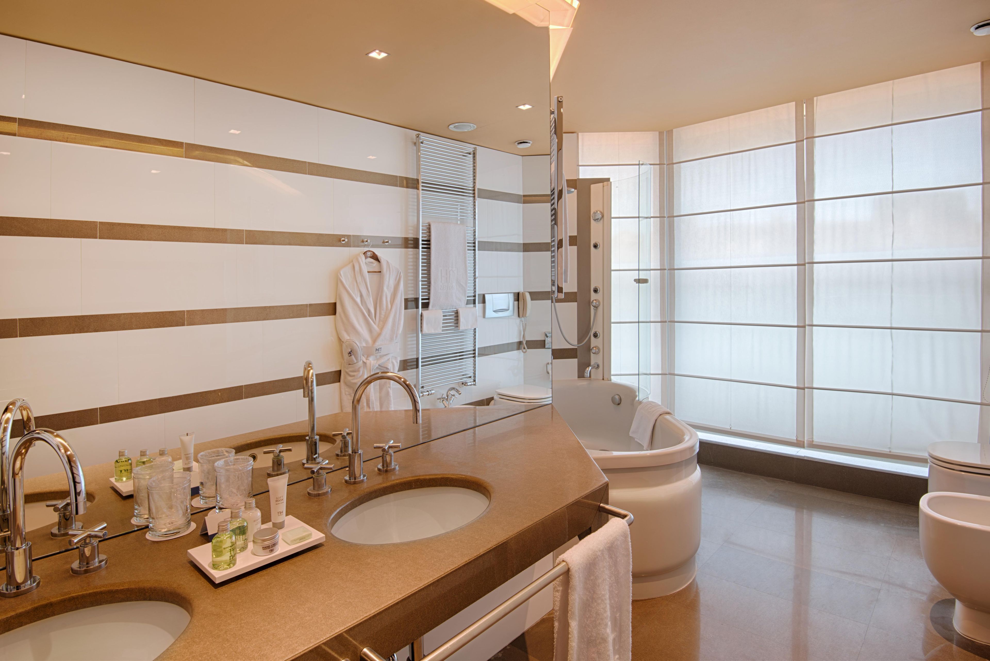 A modern bathroom with dual sinks, a large mirror, and a bathtub.