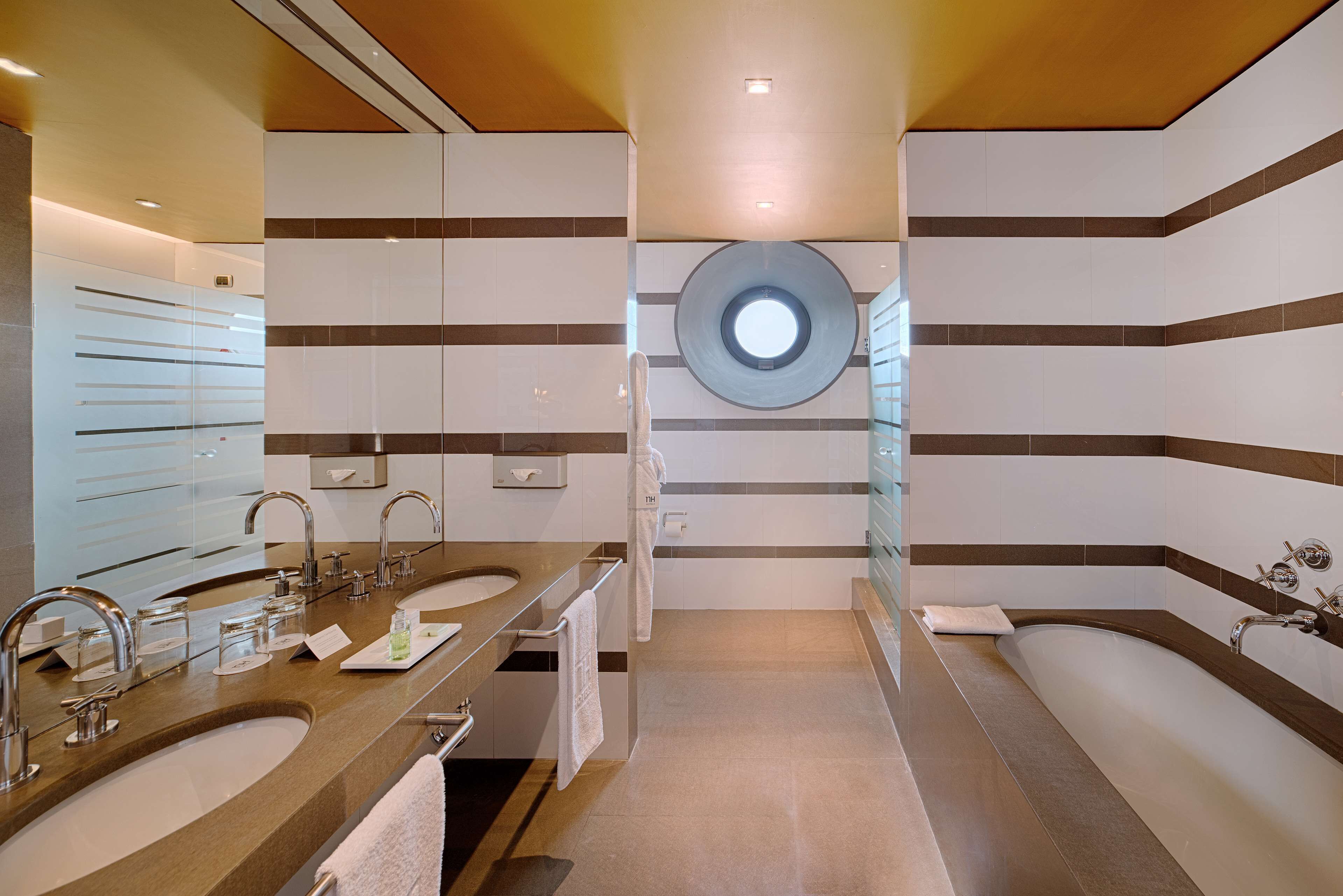 Ein modernes Badezimmer mit zwei Waschbecken, einem großen Spiegel und einem runden Dachfenster.
