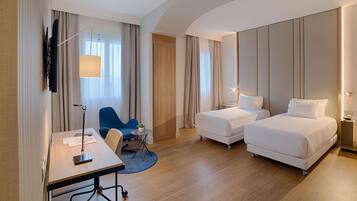 Una habitación de hotel con dos camas, un escritorio, una silla, un televisor y una lámpara.