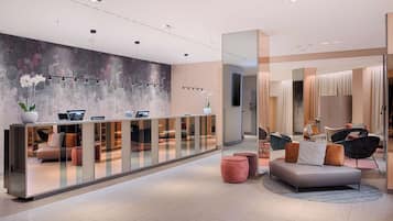 Un espace d’accueil moderne doté d’une cloison en verre, d’un coin salon avec des canapés et des fauteuils, et d’un mur décoratif orné de motifs abstraits.