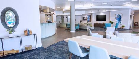 Eine moderne Hotelhalle mit Rezeption, Sitzgelegenheiten und einem großen Bildschirm.