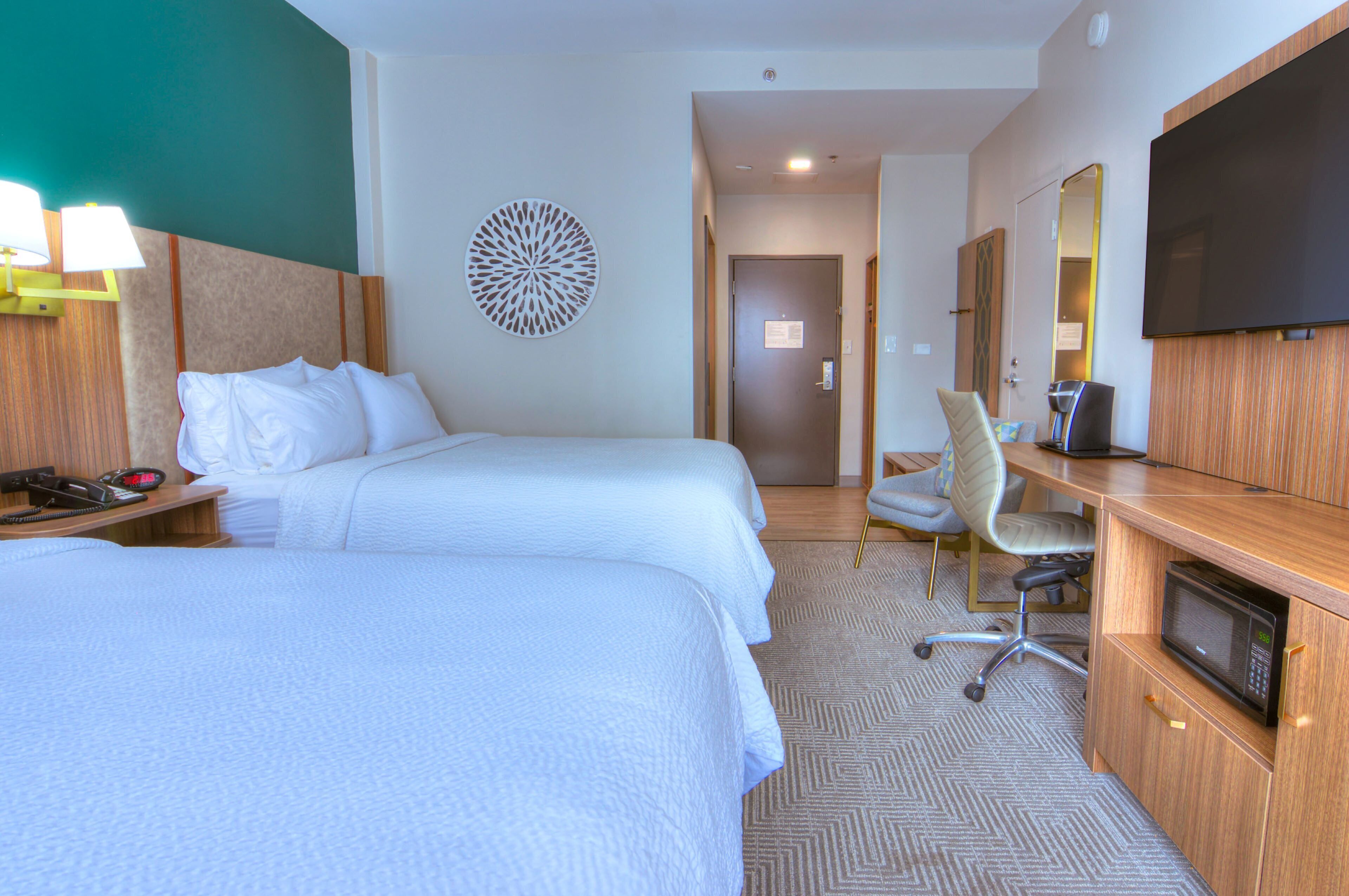 A hotel room with two beds, a desk with a computer, a TV, and a microwave.