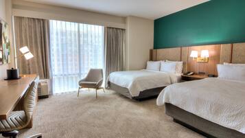 Habitación de hotel con dos camas, un escritorio, una silla, un ventanal con cortinas y una pared de acento verde.
