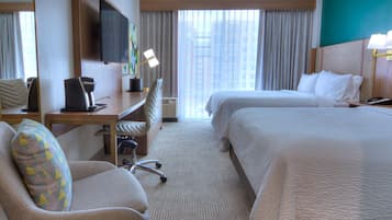 Ein Hotelzimmer mit zwei Betten, einem Schreibtisch, einem Stuhl, einem Fernseher und einem Fenster mit Vorhängen.