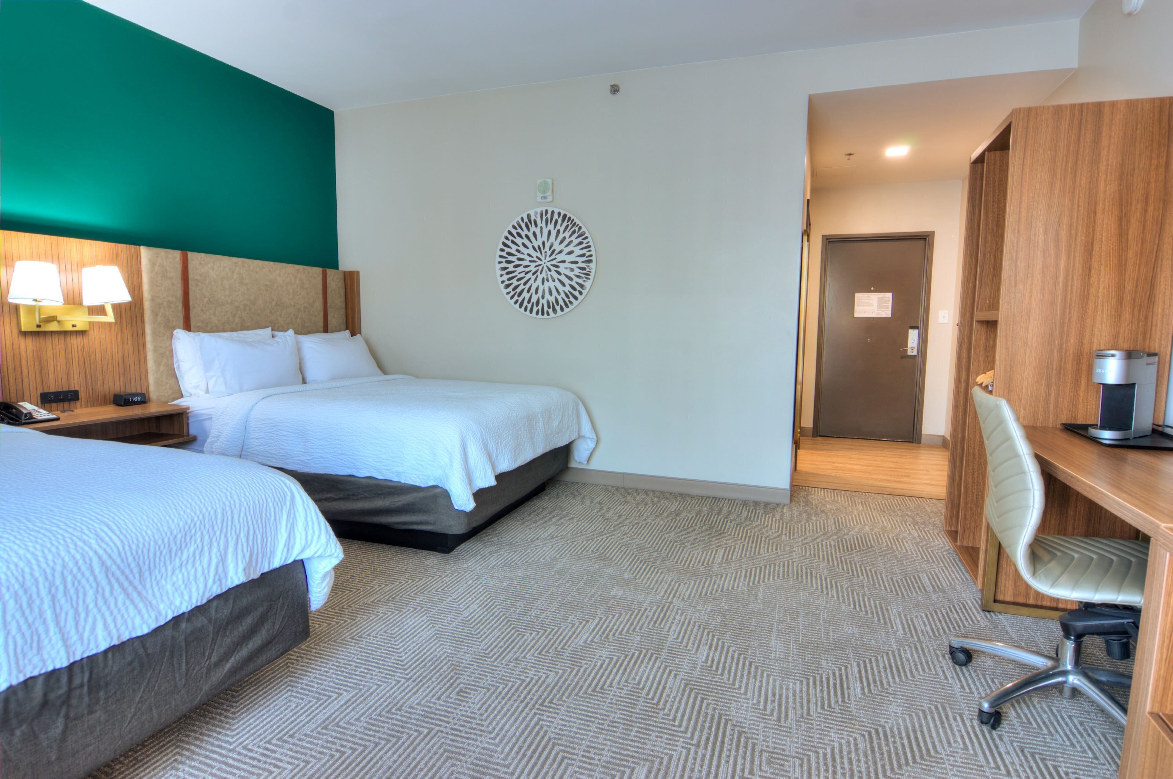 Ein Hotelzimmer mit zwei Betten, einem Schreibtisch mit Stuhl, einer Wandlampe und einem Wandbild.