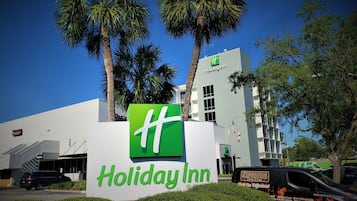 A Holiday Inn sign with a green logo, palm trees, and a building with multiple windows.