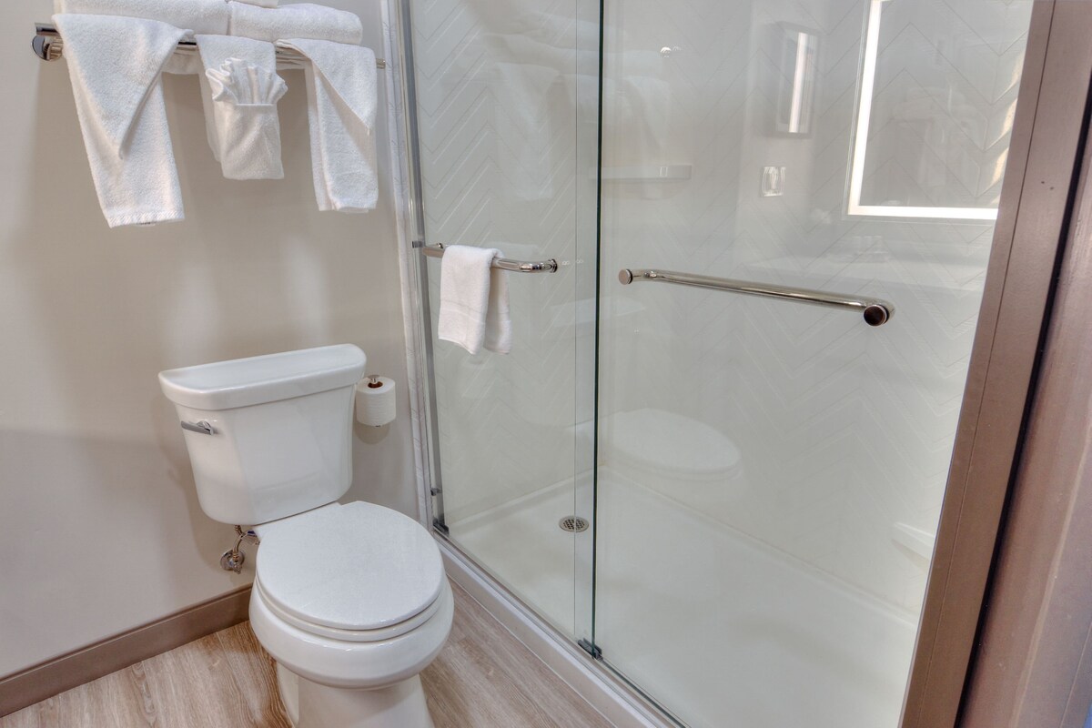 Une salle de bain moderne avec une douche à parois de verre, des toilettes blanches et un porte-serviettes avec plusieurs serviettes.
