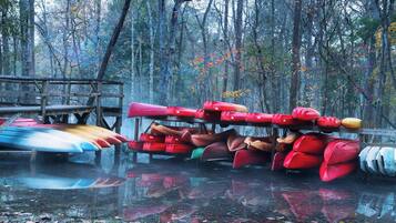 Varias kayaks y canoas apiladas sobre una plataforma de madera en un área boscosa.