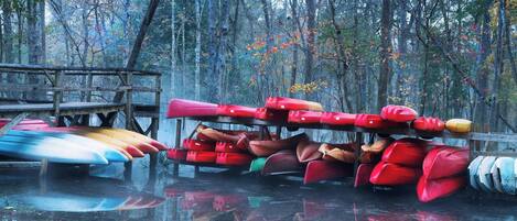 A collection of kayaks and canoes stacked on a wooden platform in a forested area.