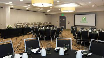 Une salle de conférence avec des tables disposées pour une réunion, équipée d’ordinateurs portables et d’un écran affichant le logo de Holiday Inn.