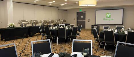 Une salle de conférence avec des tables disposées pour une réunion, équipée d’ordinateurs portables et d’un écran affichant le logo de Holiday Inn.