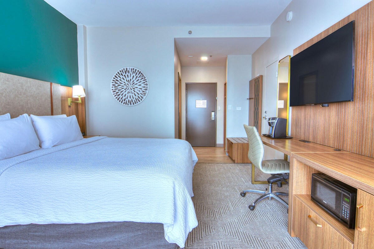 A hotel room with a large bed, a desk with a flat-screen TV, a microwave, and a chair.