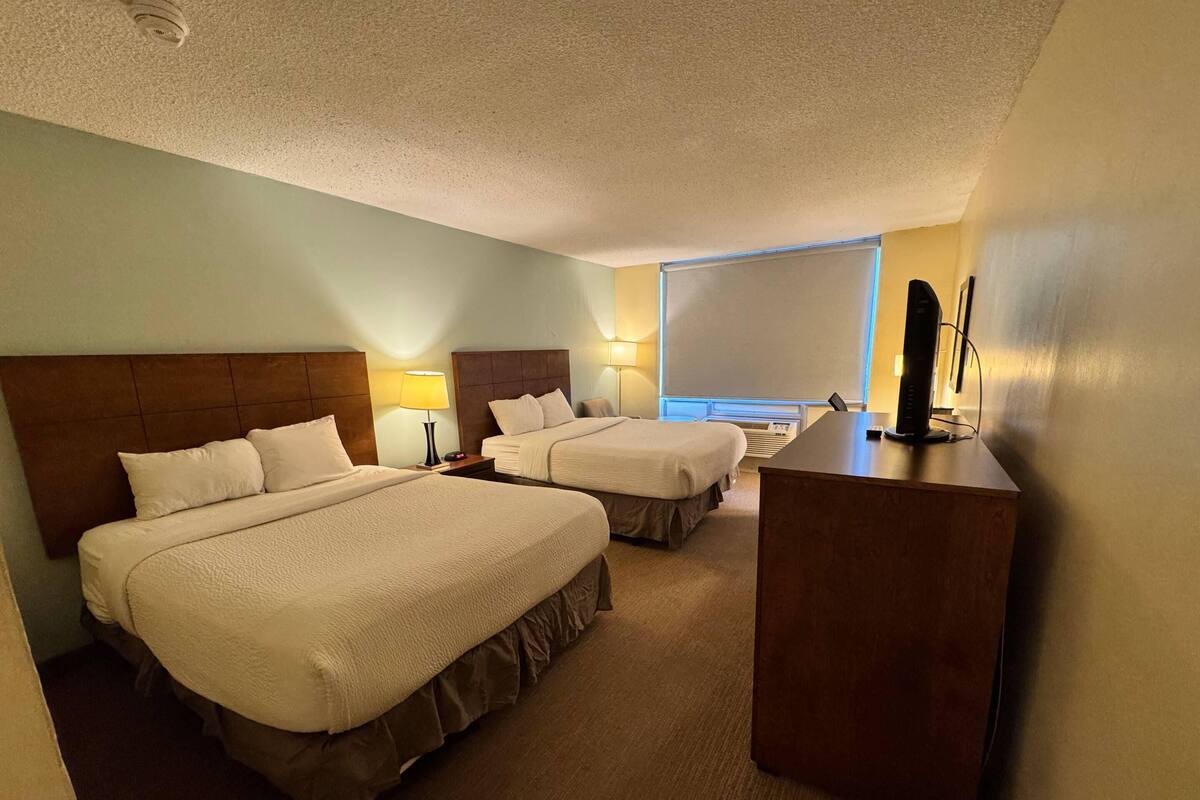 Une chambre d’hôtel avec deux lits, un bureau, une lampe et une grande fenêtre.