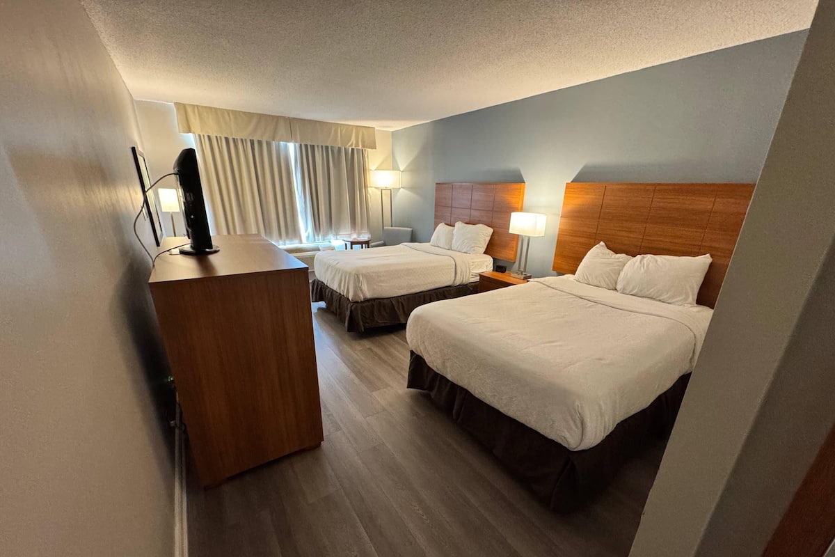 Une chambre d’hôtel avec deux lits, un bureau, une lampe et une vue sur l’extérieur.