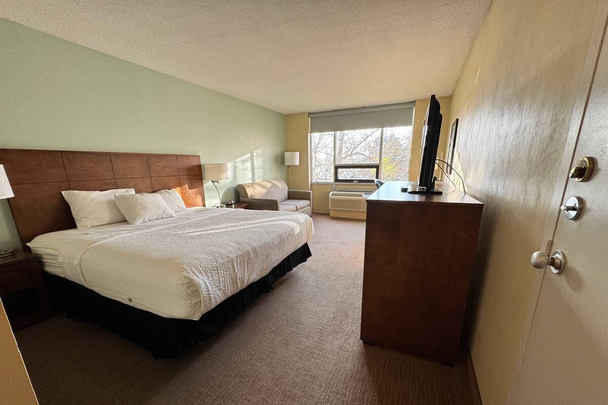 Une chambre d’hôtel avec un lit, des tables de chevet, un bureau, une chaise et une fenêtre donnant sur un paysage agréable.
