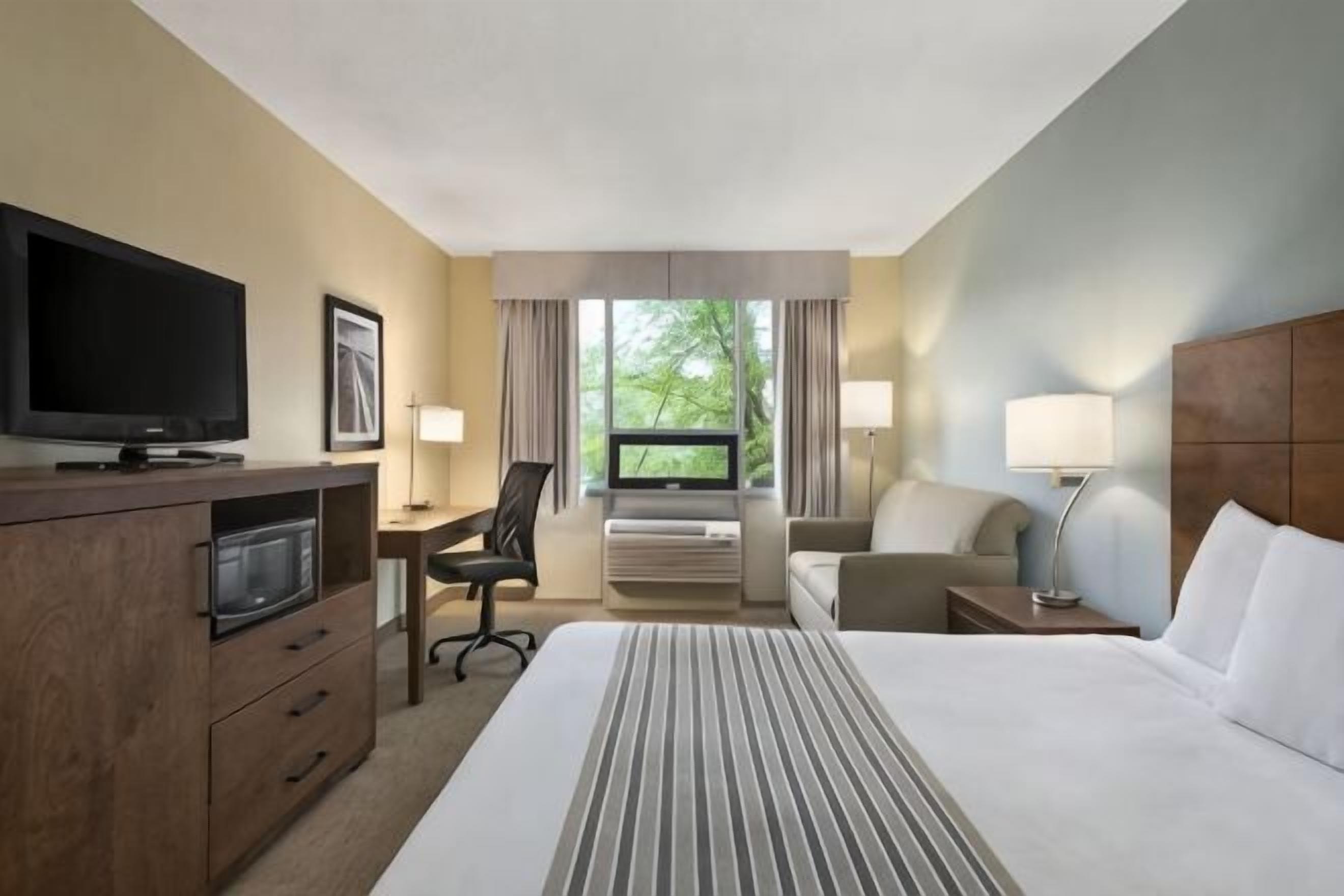 A hotel room with a bed, a desk, a television, a chair, and a window with curtains.