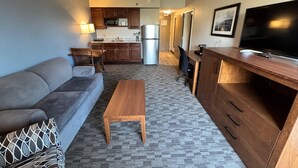 A compact living space with a sofa, a wooden coffee table, a TV, a kitchenette, and a dining area. - Quality Inn & Suites (Sydney)