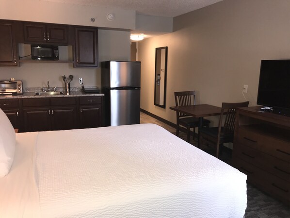 A hotel room with a bed, a kitchenette, a dining table, and a TV.