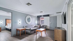 Een moderne hotelkamer met een grijze bank, een houten bijzettafeltje en een televisie op een houten kast.