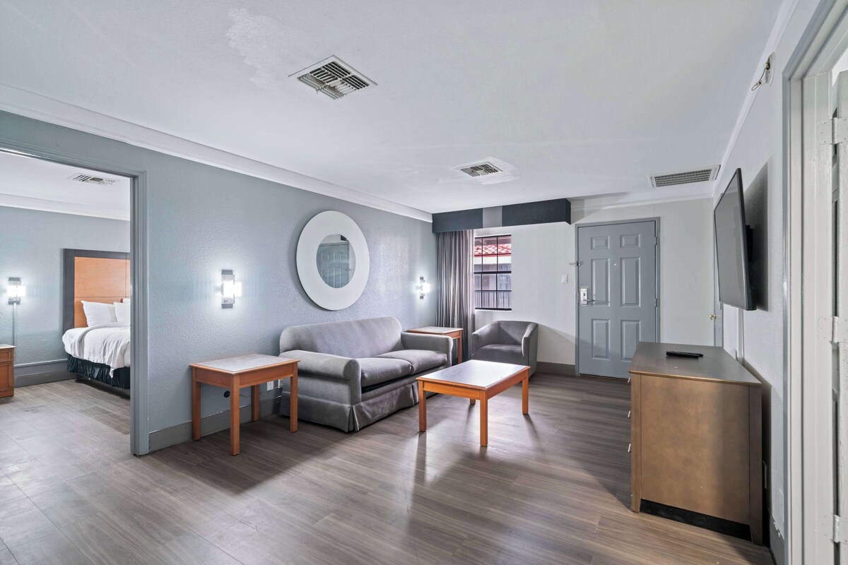 A modern hotel room with a grey sofa, wooden coffee table, and a TV on a wooden cabinet.