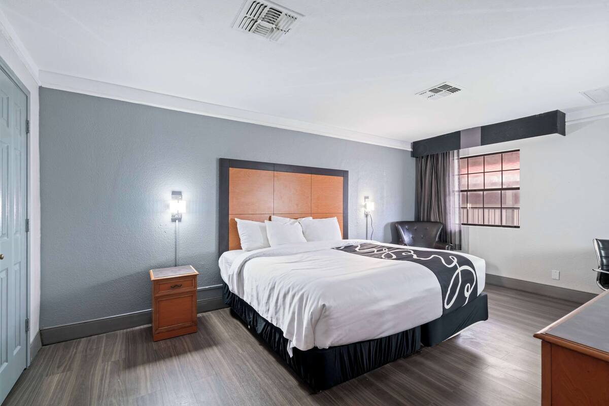 Une chambre d’hôtel moderne avec un grand lit, une table de chevet, un bureau et une fenêtre avec des rideaux.