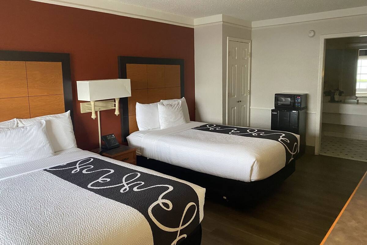Une chambre d’hôtel avec deux lits, une table de chevet avec une lampe, une télévision et une porte donnant sur une salle de bain.